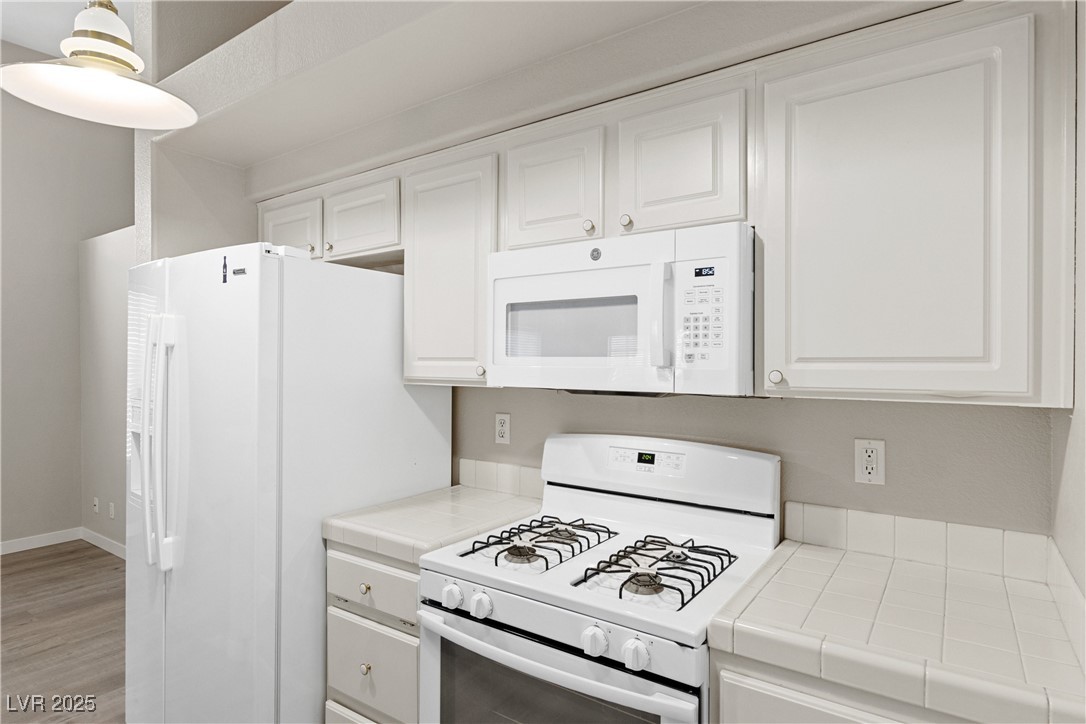 5240 Island Chain Road Las Vegas, NV 89118 - Photo 8 of 26 Kitchen featuring white appliances, tile countertops, white cabinets, and light wood finished floors