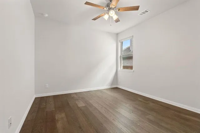 an empty room with wooden floor fan and windows