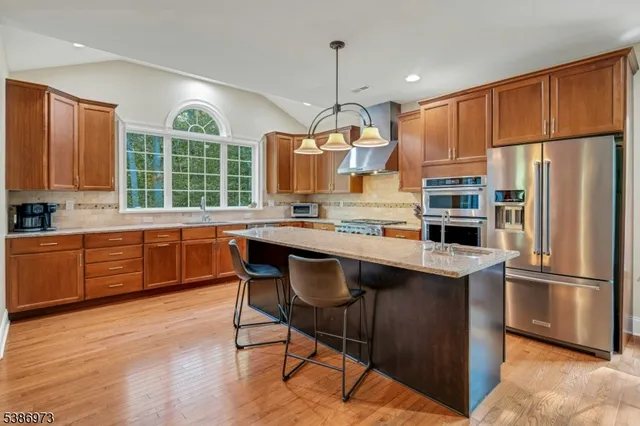 a kitchen with kitchen island granite countertop wooden floors stainless steel appliances a sink and a window