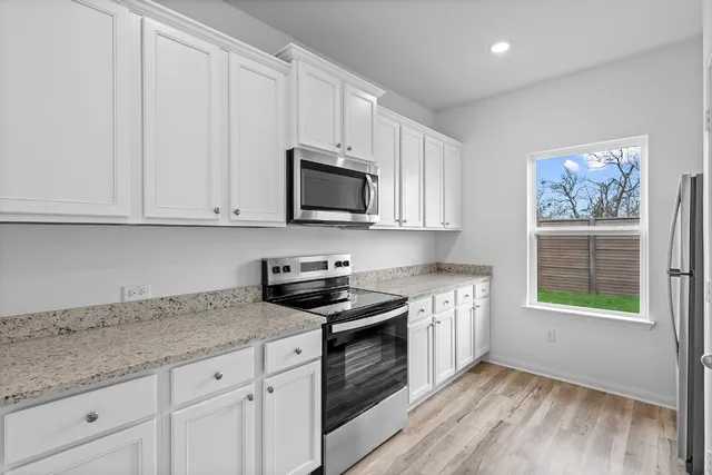 a kitchen with granite countertop white cabinets stainless steel appliances a sink and wooden floor