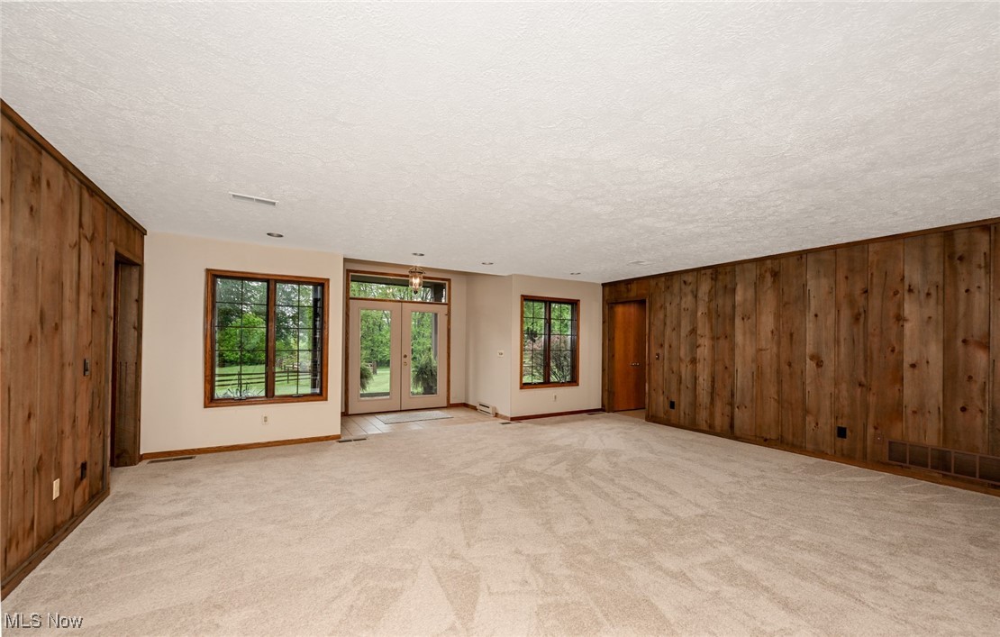 4010 State Road Medina, OH 44256 - Photo 10 of 50 Empty room featuring wooden walls, healthy amount of natural light, light carpet, a textured ceiling, and baseboards