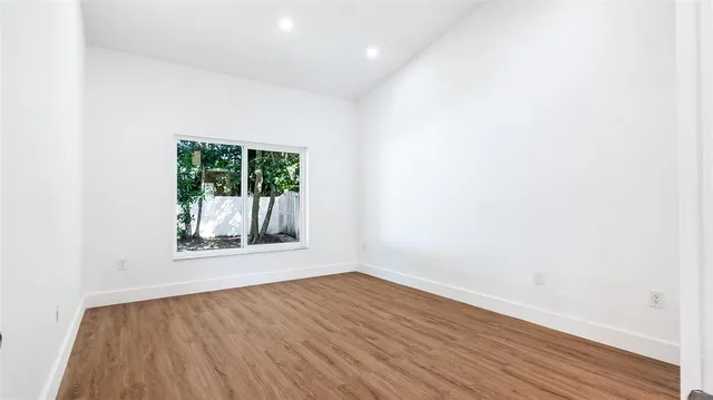 a view of an empty room with wooden floor and a window