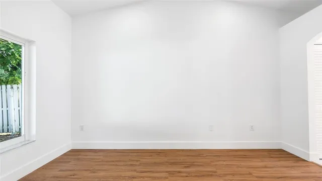 a view of an empty room with wooden floor and a window