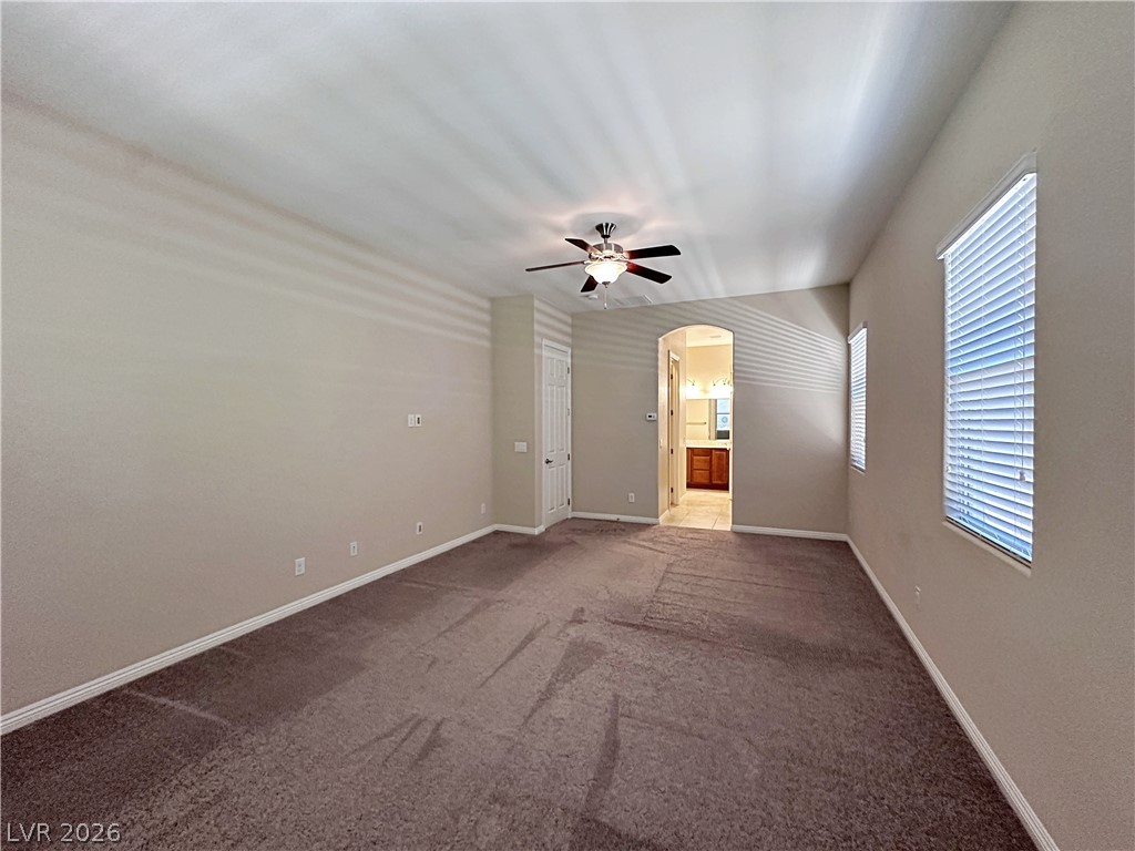 71 Newton Ridge Way Las Vegas, NV 89183 - Photo 27 of 40 A spacious primary bedroom with a cooling ceiling fan and abundant natural illumination through multiple windows.