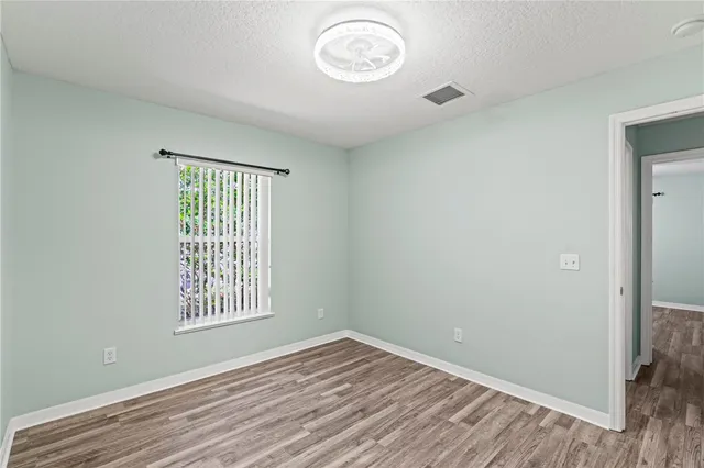 an empty room with wooden floor fan and windows