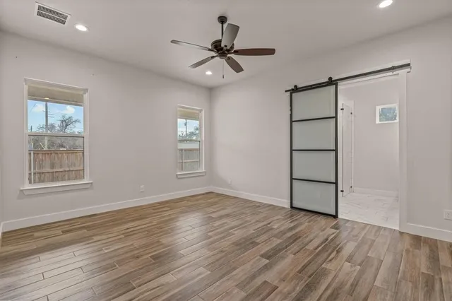 an empty room with wooden floor chandelier fan and windows