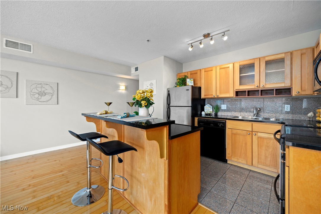 2222 Detroit Avenue, Unit 519 Cleveland, OH 44113 - Photo 8 of 30 Kitchen featuring a kitchen bar, stainless and black appliances, decorative backsplash, and granite tile flooring