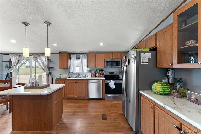 a kitchen with stainless steel appliances granite countertop a refrigerator a sink dishwasher a stove and a dining table with wooden floor