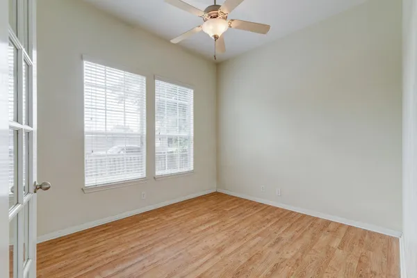 an empty room with wooden floor fan and windows