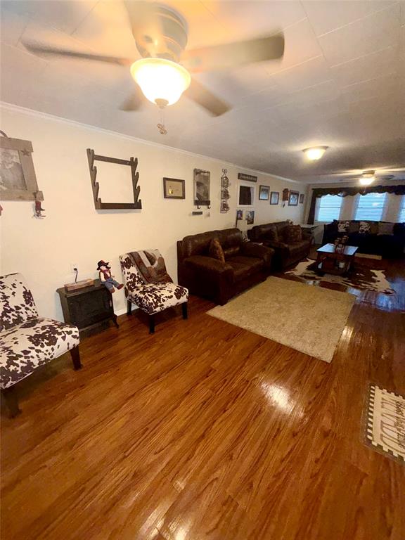 309 Broken Arrow Comanche, TX 76442 - Photo 20 of 33 Living area with dark wood-type flooring, crown molding, and a ceiling fan