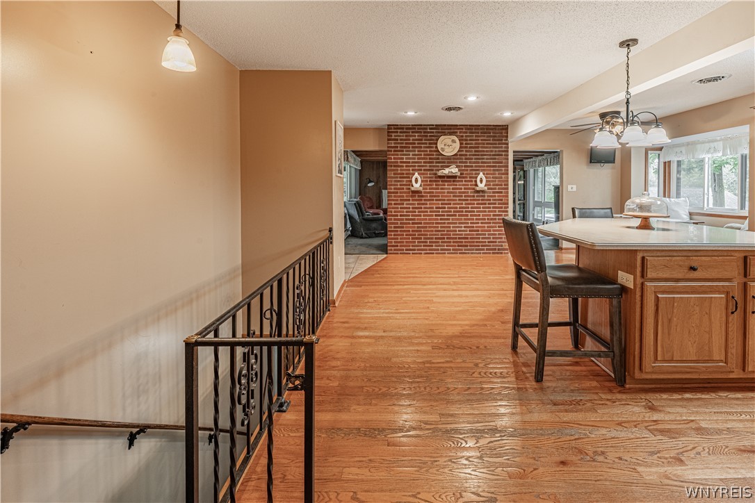 6775 Bear Ridge Road Pendleton, NY 14094 - Photo 16 of 48 Rich hardwood floors lead past a wrought-iron stair railing toward a classic brick accent wall.