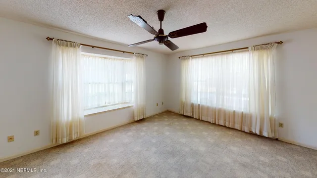 an empty room with windows and chandelier fan