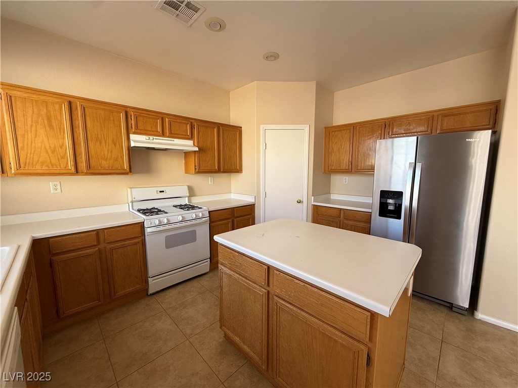 9950 Shadow Grove Avenue Las Vegas, NV 89148 - Photo 12 of 37 Kitchen featuring white appliances, light tile patterned floors, brown cabinetry, and light countertops