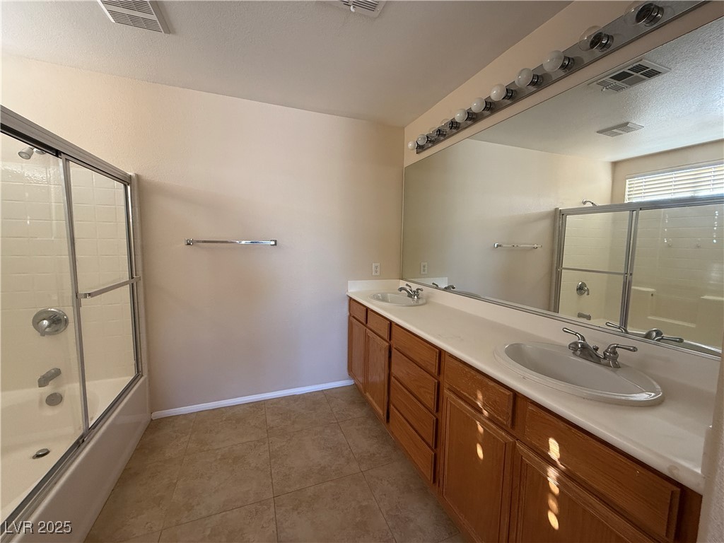 9950 Shadow Grove Avenue Las Vegas, NV 89148 - Photo 18 of 37 Full bathroom with bath / shower combo with glass door, double vanity, light tile patterned floors, and a textured ceiling