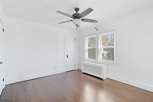 an empty room with wooden floor chandelier fan and windows