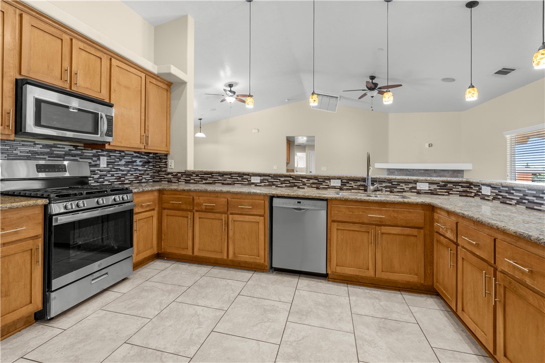 8755 Lilac Road Oak Hills, CA 92344 - Photo 9 of 28 a large kitchen with stainless steel appliances granite countertop a stove a sink and a microwave