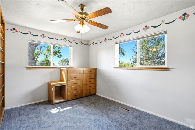 2252 West 800 North Clinton, UT 84015 - Photo 15 of 38 Light-filled room featuring two windows, blue carpeting, and a ceiling fan with integrated lighting