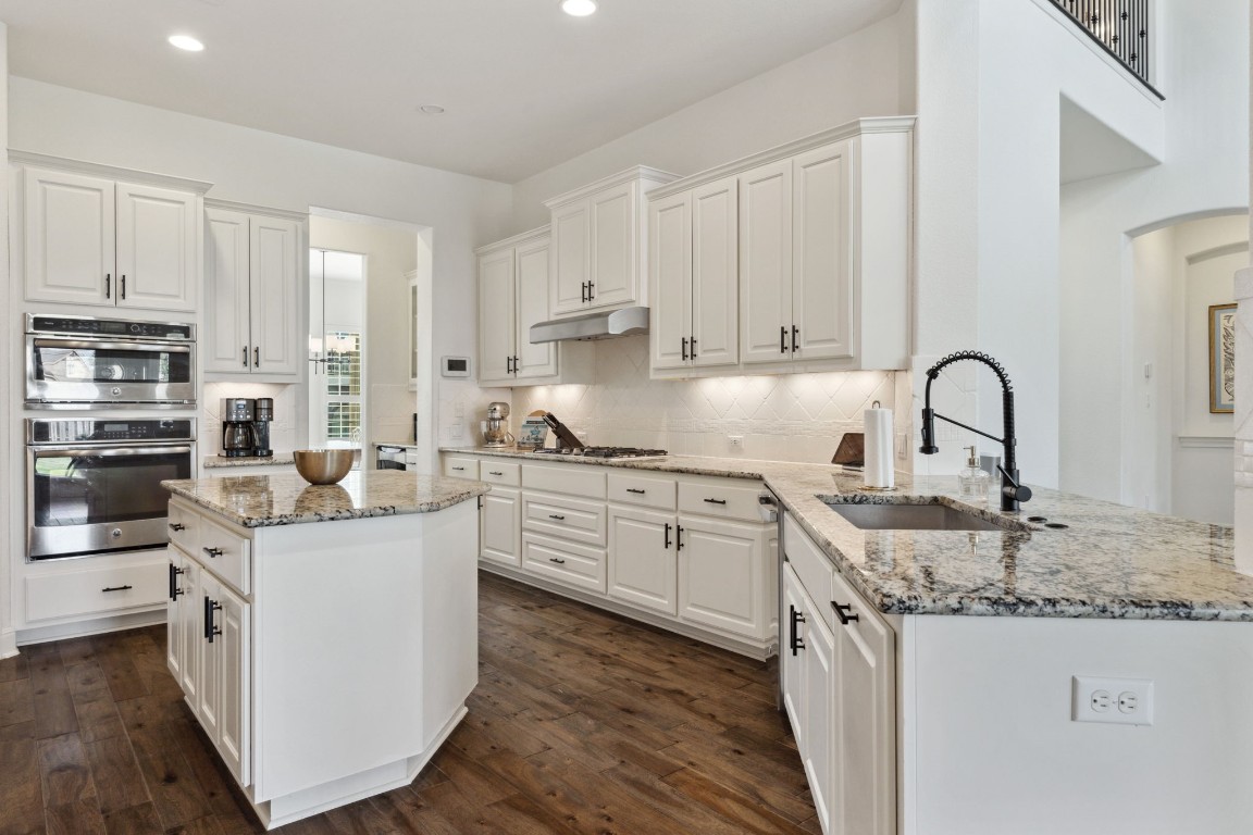 a kitchen with stainless steel appliances granite countertop a stove a sink dishwasher and white cabinets with wooden floor
