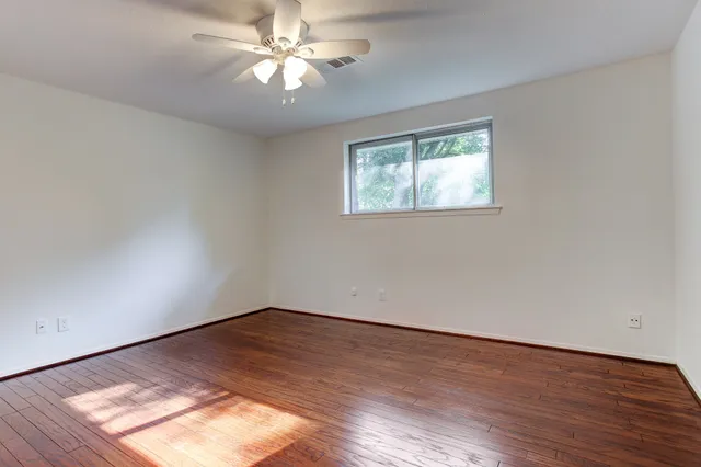 an empty room with wooden floor chandelier fan and windows