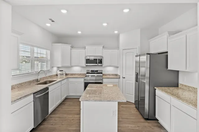 a kitchen with stainless steel appliances granite countertop a stove top oven a refrigerator a sink and dishwasher with wooden floor