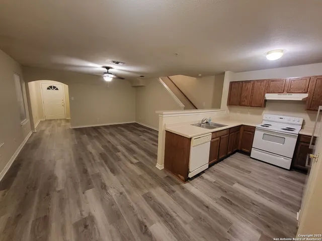 an empty room with wooden floor chandelier fan and windows