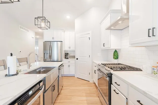 a kitchen with stainless steel appliances a sink dishwasher and white cabinets with wooden floor
