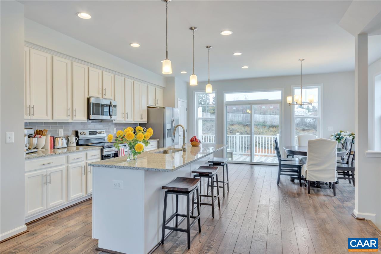 a kitchen with stainless steel appliances granite countertop a stove top oven a sink a dining table and chairs with wooden floor