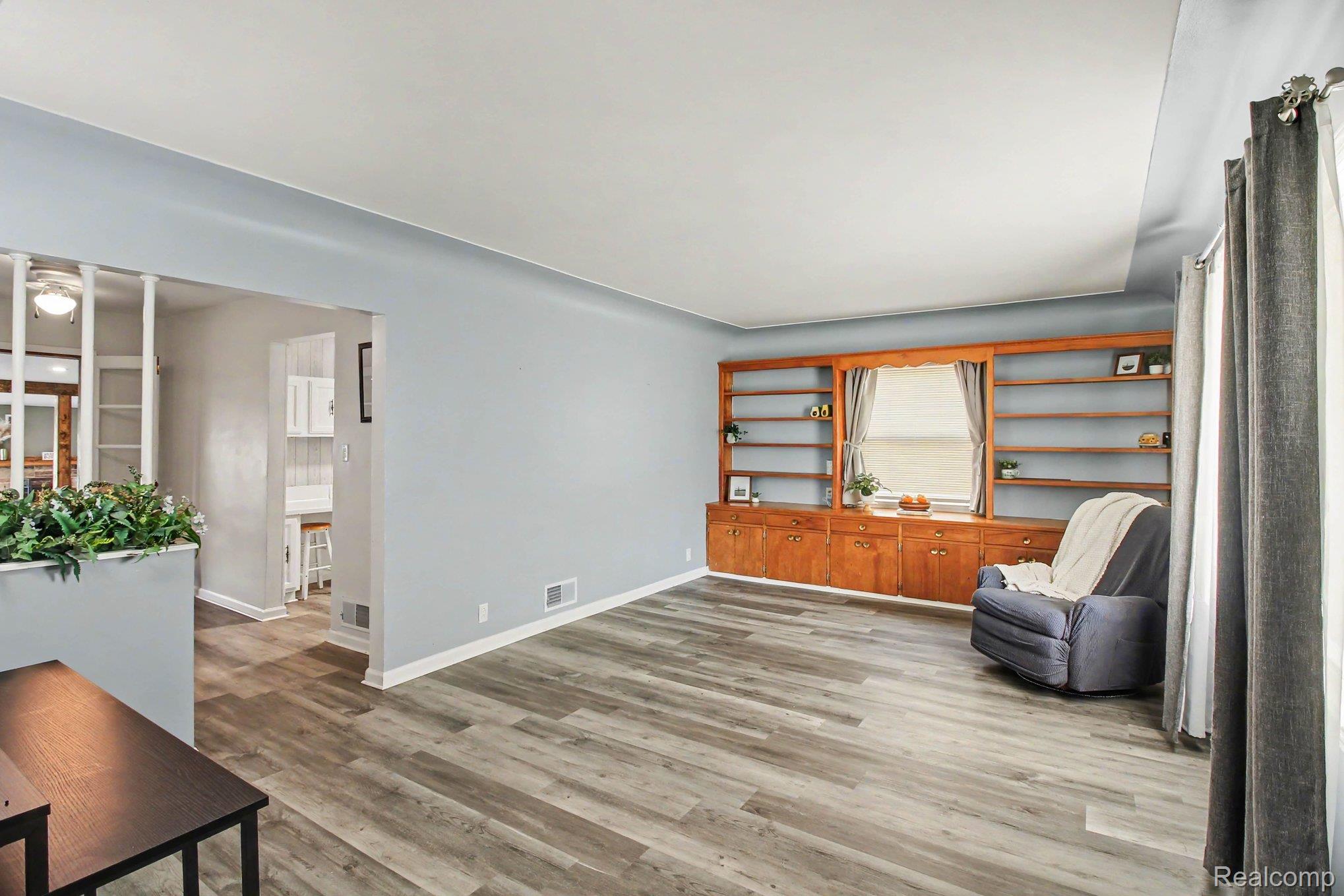 207 Elms Road Flushing, MI 48433 - Photo 3 of 30 Wood-finish flooring throughout, light blue wall paint, and a built-in wood shelving unit with lower cabinetry