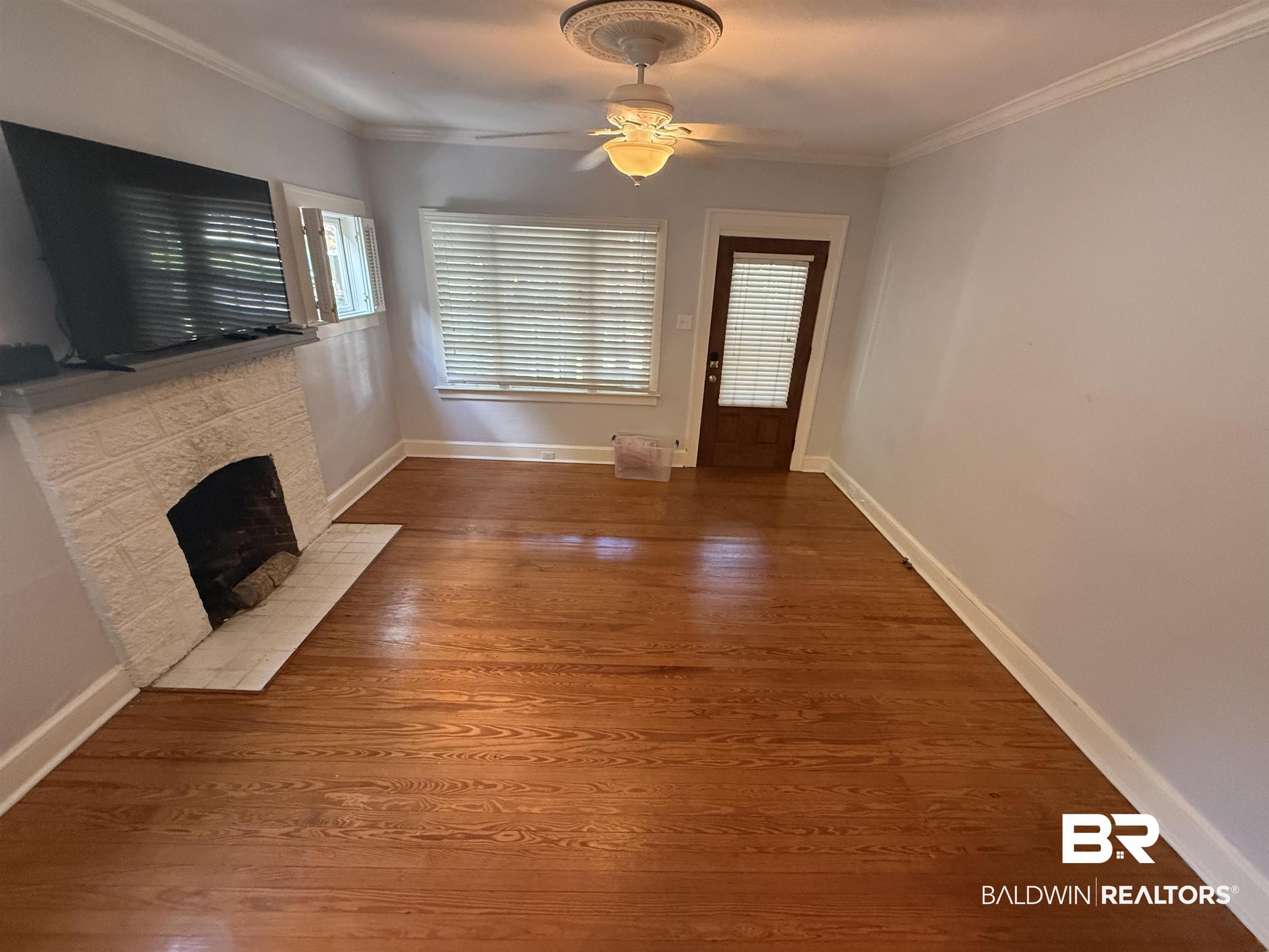 266 Westwood Street Mobile, AL 36606 - Photo 30 of 34 Unfurnished living room with a ceiling fan, crown molding, a stone fireplace, and wood finished floors