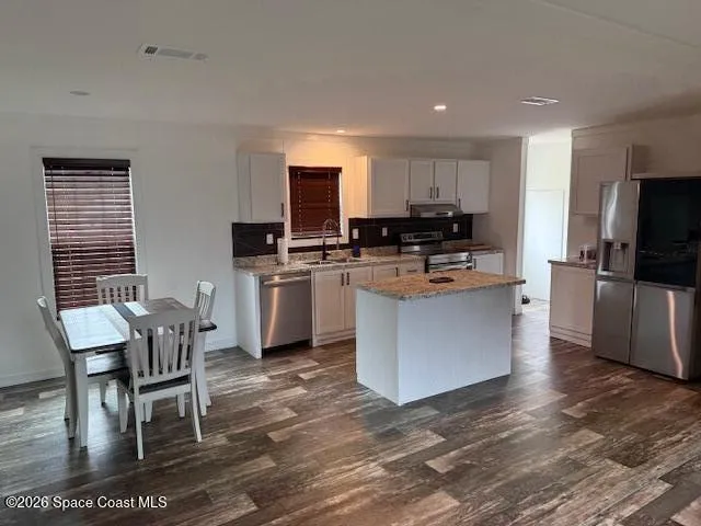 a kitchen with stainless steel appliances granite countertop a stove top oven a sink dishwasher a dining table and chairs with wooden floor