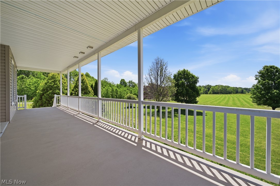 12159 Lawndell Road Southwest Beach City, OH 44608 - Photo 5 of 49 Expansive covered porch featuring a white railing system, recessed lighting, and a neutral-toned floor, overlooking a substantial green lawn and mature trees