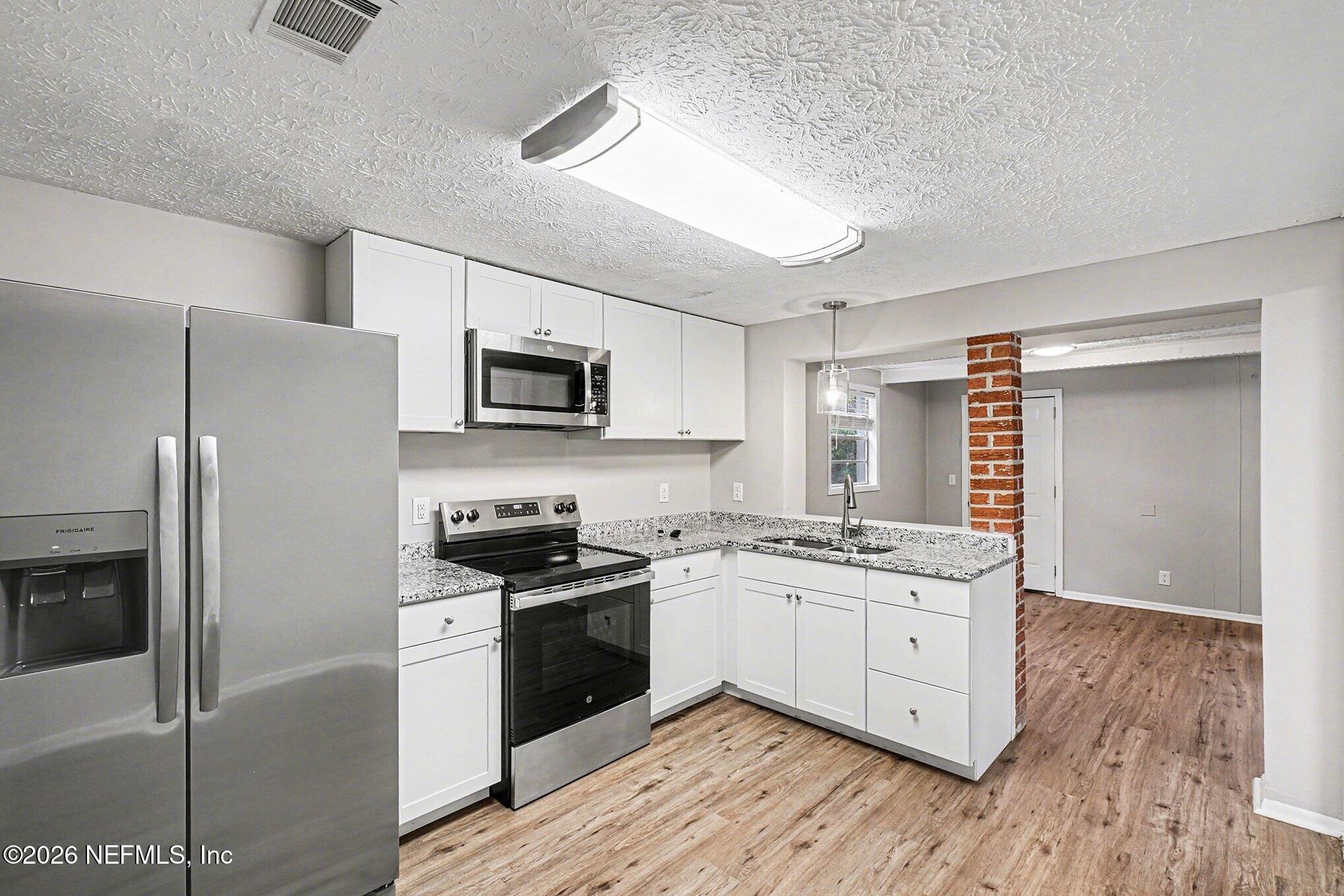 8417 Barracuda Road Jacksonville, FL 32244 - Photo 7 of 15 a kitchen with stainless steel appliances granite countertop a stove top oven a sink a refrigerator white cabinets and wooden floor