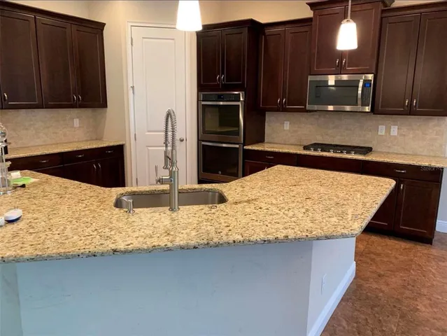 a kitchen with kitchen island granite countertop wooden cabinets refrigerator and microwave
