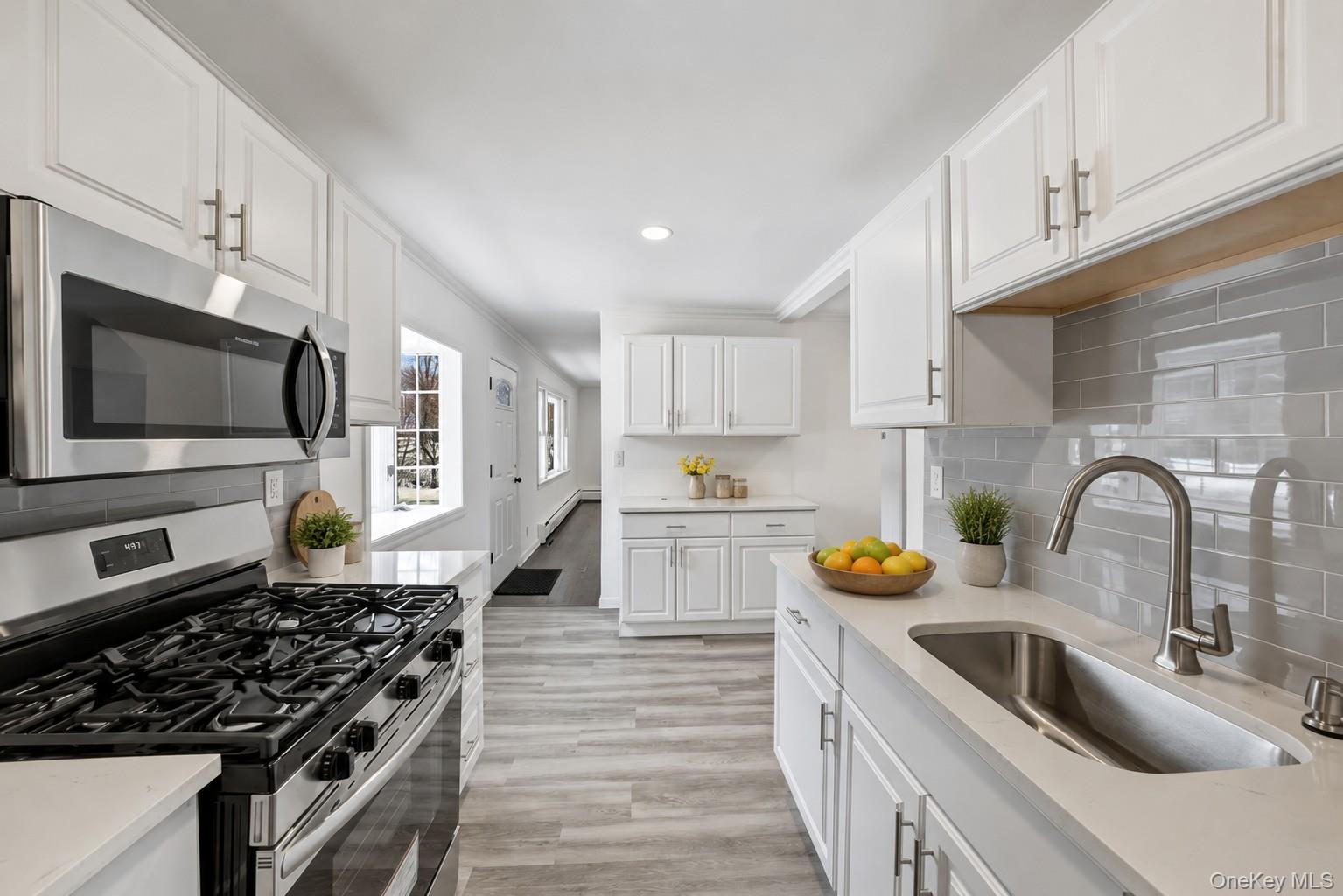 785 Locksley Road Yorktown Heights, NY 10598 - Photo 2 of 16 Modern kitchen featuring white shaker cabinetry, stainless steel appliances including a gas range and microwave, light gray subway tile backsplash, and wood-finish flooring photos have been digitally enhanced to illustrate the property's potential.
