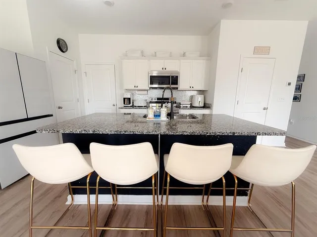 a kitchen with stainless steel appliances kitchen island granite countertop a dining table chairs and a refrigerator