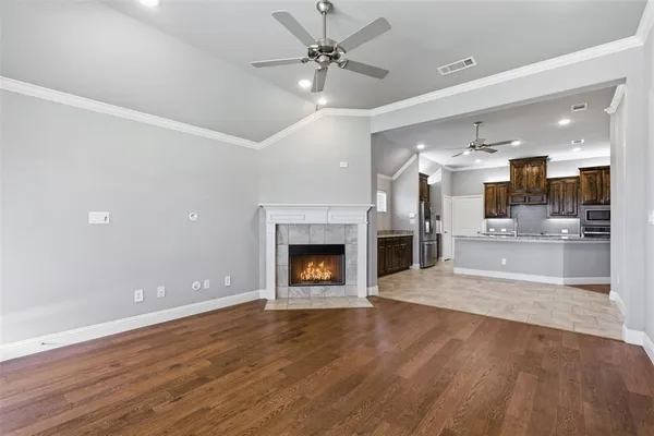 an empty room with wooden floor fireplace and a kitchen view