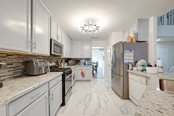 a kitchen with stainless steel appliances granite countertop a refrigerator a sink dishwasher a stove and white cabinets with wooden floor