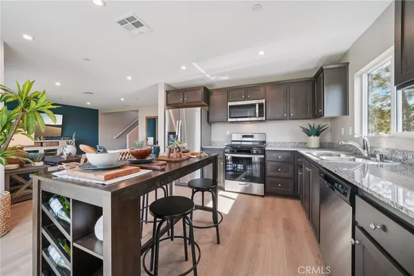 a kitchen with stainless steel appliances granite countertop a stove a sink dishwasher a microwave oven and a dining table with wooden floor