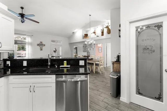 a kitchen with stainless steel appliances granite countertop a sink dishwasher a refrigerator and white cabinets with wooden floor