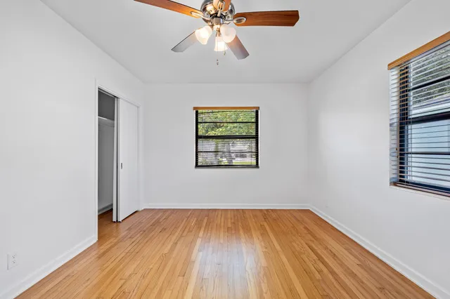 an empty room with wooden floor chandelier fan and windows