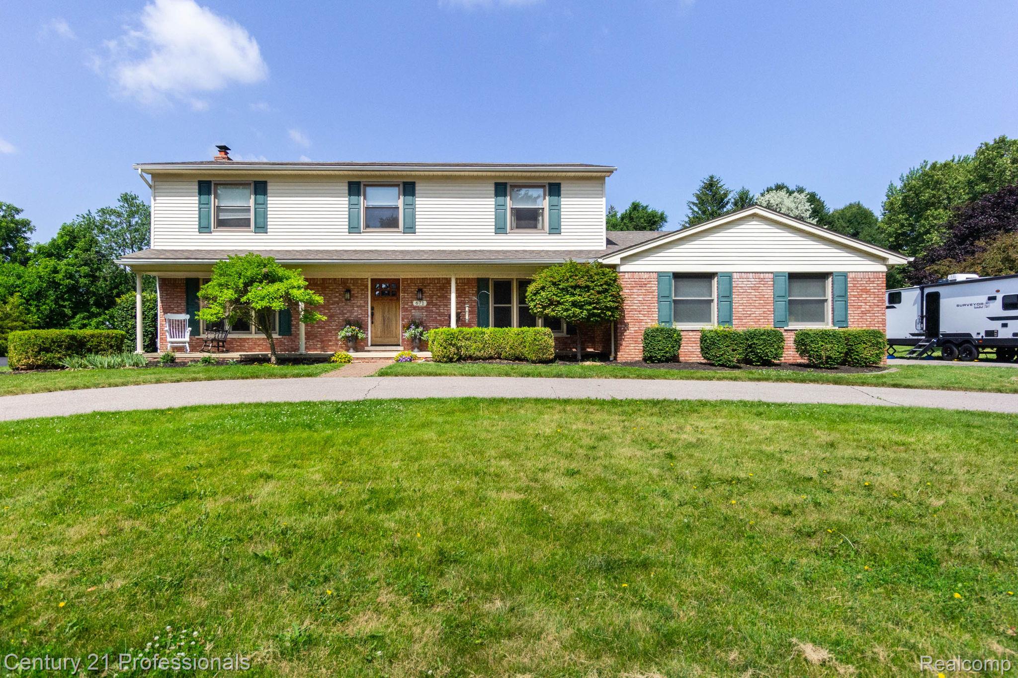 671 Bridgestone Drive Rochester, MI 48309 - Photo 1 of 50 Traditional two-story residence with brick and siding exterior, featuring a covered front porch, green shutters, a paved driveway, and established front landscaping