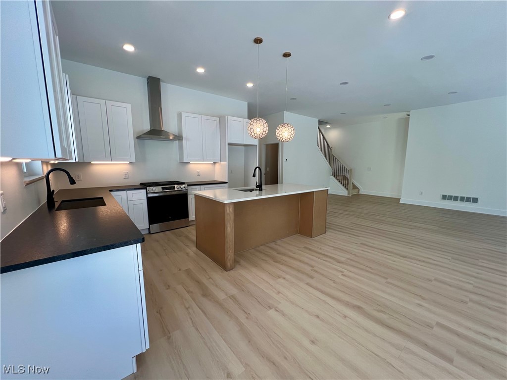 Kitchen featuring shaker white cabinetry, new stainless steel appliances, a center island, wall chimney range hood, and sink