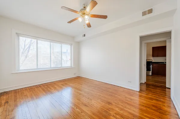 an empty room with wooden floor chandelier fan and windows
