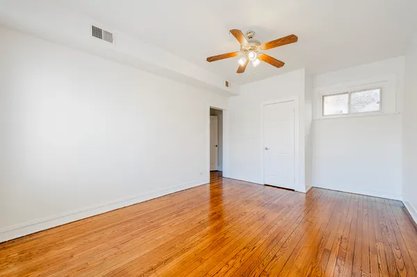 a view of an empty room with wooden floor and a ceiling fan