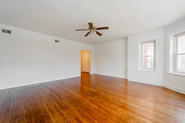 an empty room with wooden floor ceiling fan and windows
