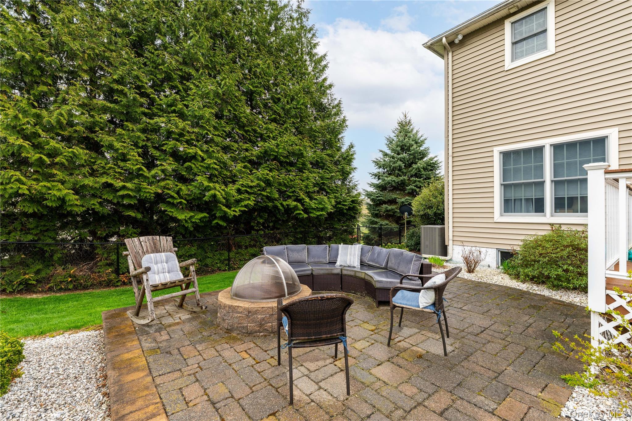 60 Idlewild Road Marlboro, NY 12542 - Photo 5 of 37 Paver patio with a built-in stone fire pit, bordered by a gravel path and mature evergreen trees