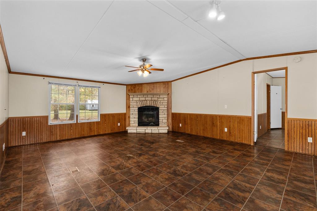 334 Destiny Lane Keatchie, LA 71046 - Photo 5 of 29 Unfurnished living room featuring a wainscoted wall, a fireplace, a ceiling fan, wood walls, and ornamental molding