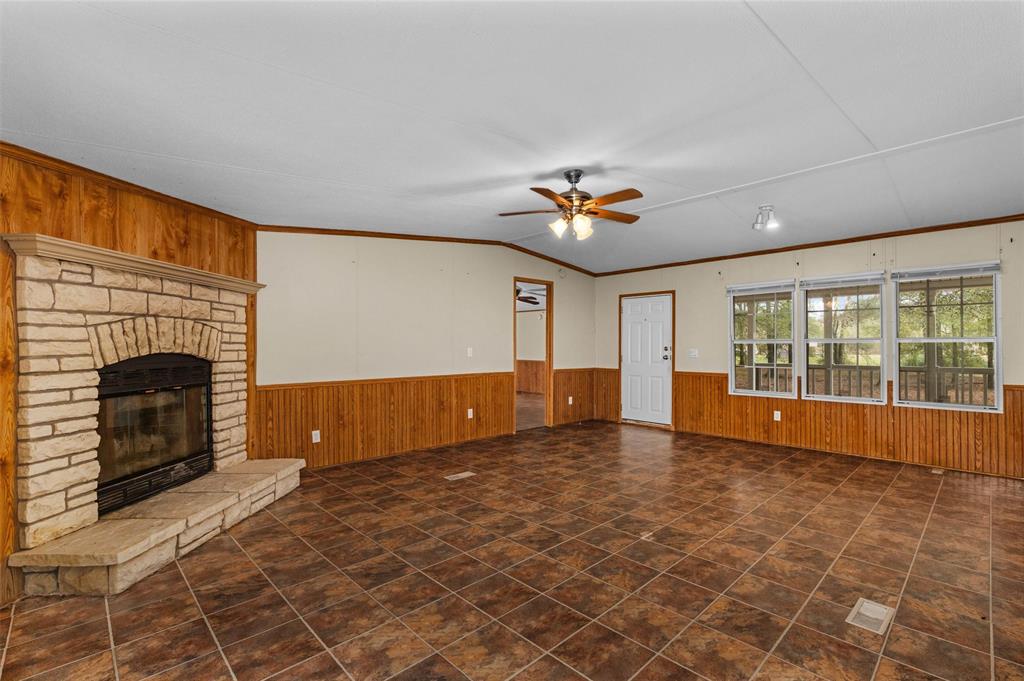 334 Destiny Lane Keatchie, LA 71046 - Photo 7 of 29 Unfurnished living room with ornamental molding, wood walls, a brick fireplace, a wainscoted wall, and ceiling fan