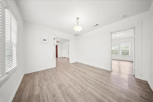an empty room with wooden floor chandelier and windows