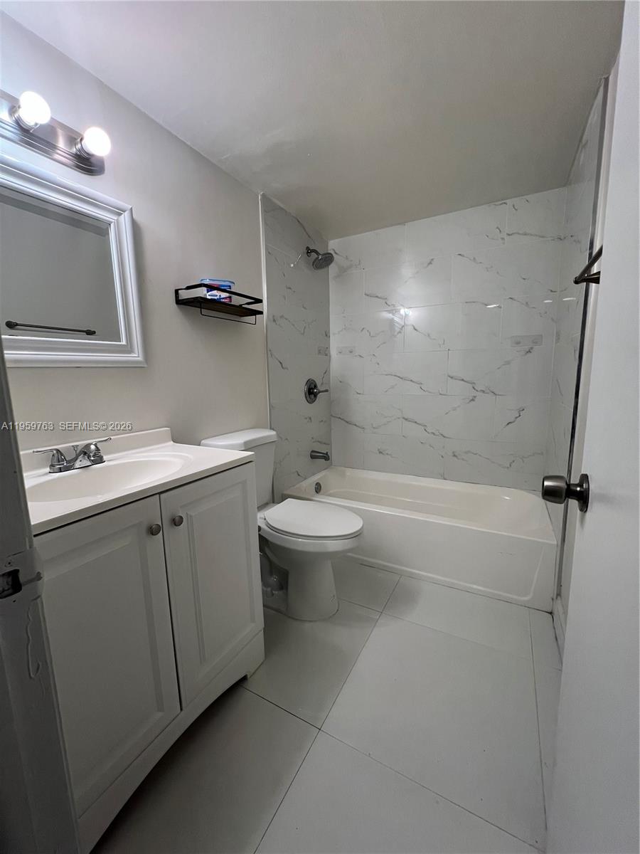 14155 Southwest 87th Street, Unit E201 Miami, FL 33183 - Photo 9 of 14 a bathroom with a double vanity sink toilet mirror and shower